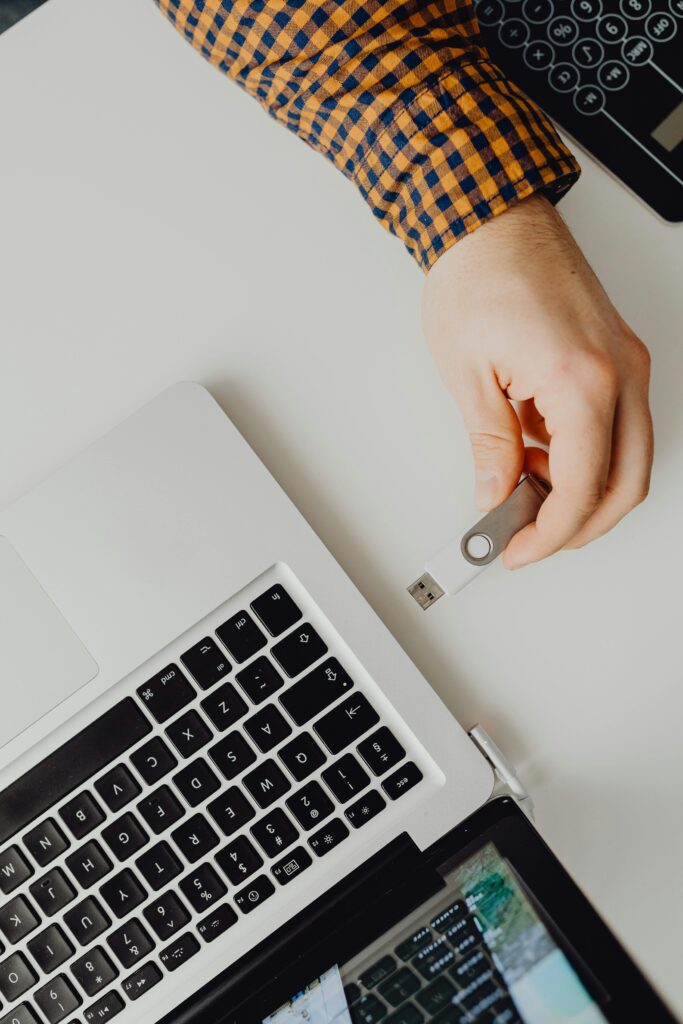 Hand inserting USB flash drive into a laptop, view from above.